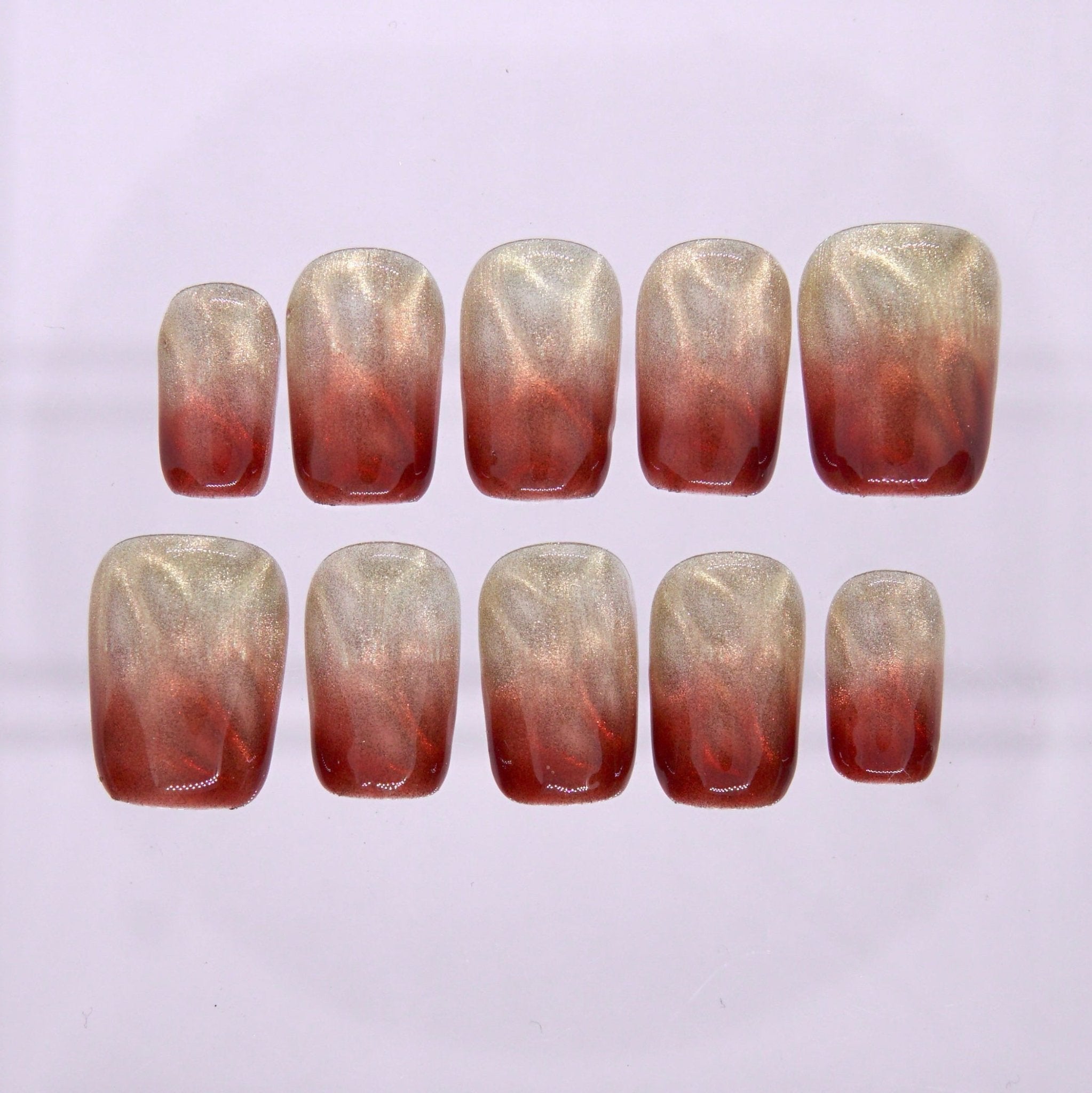 Short square press on nails with champagne cat eye shimmer and red brown ombré gradient on a glossy finish
