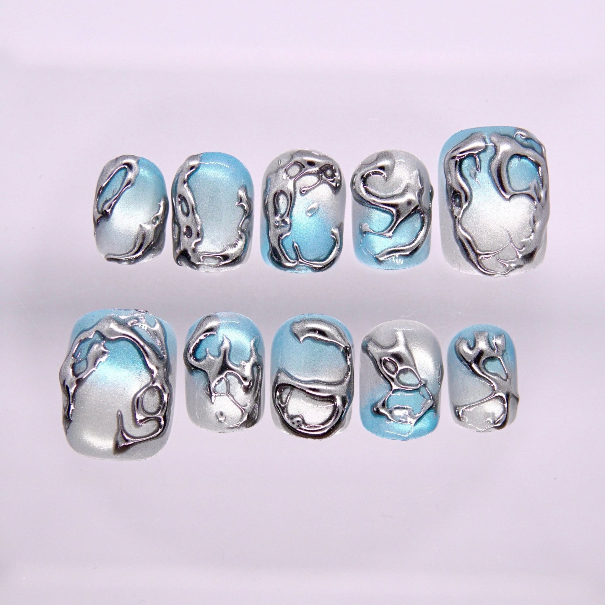 Begin in Motion press-on nails set featuring blue and silver tones with fluid metallic line design inspired by movement