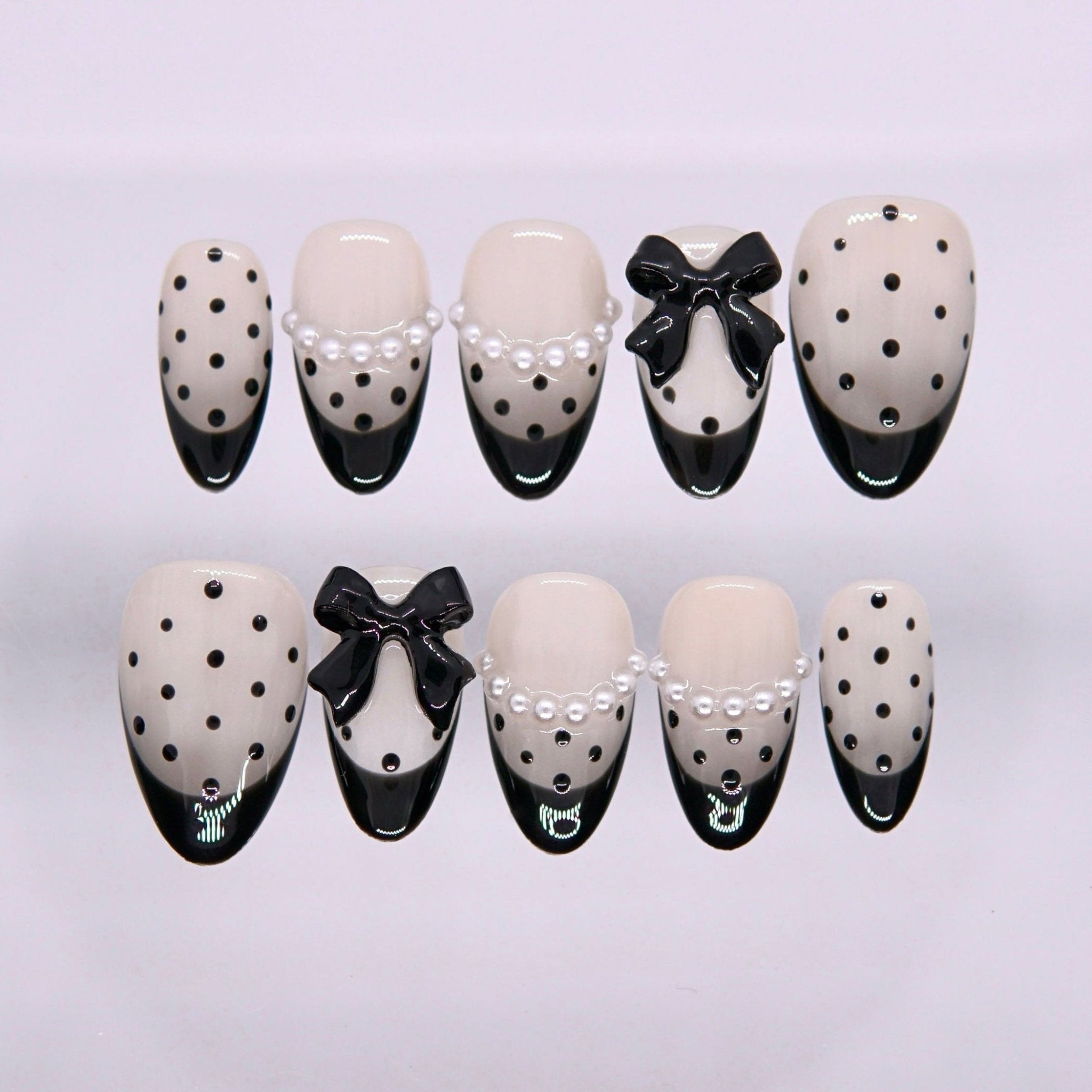 Begin with Intention press-on nails set featuring black and ivory tones with polka dots, pearl accents, and bow details
