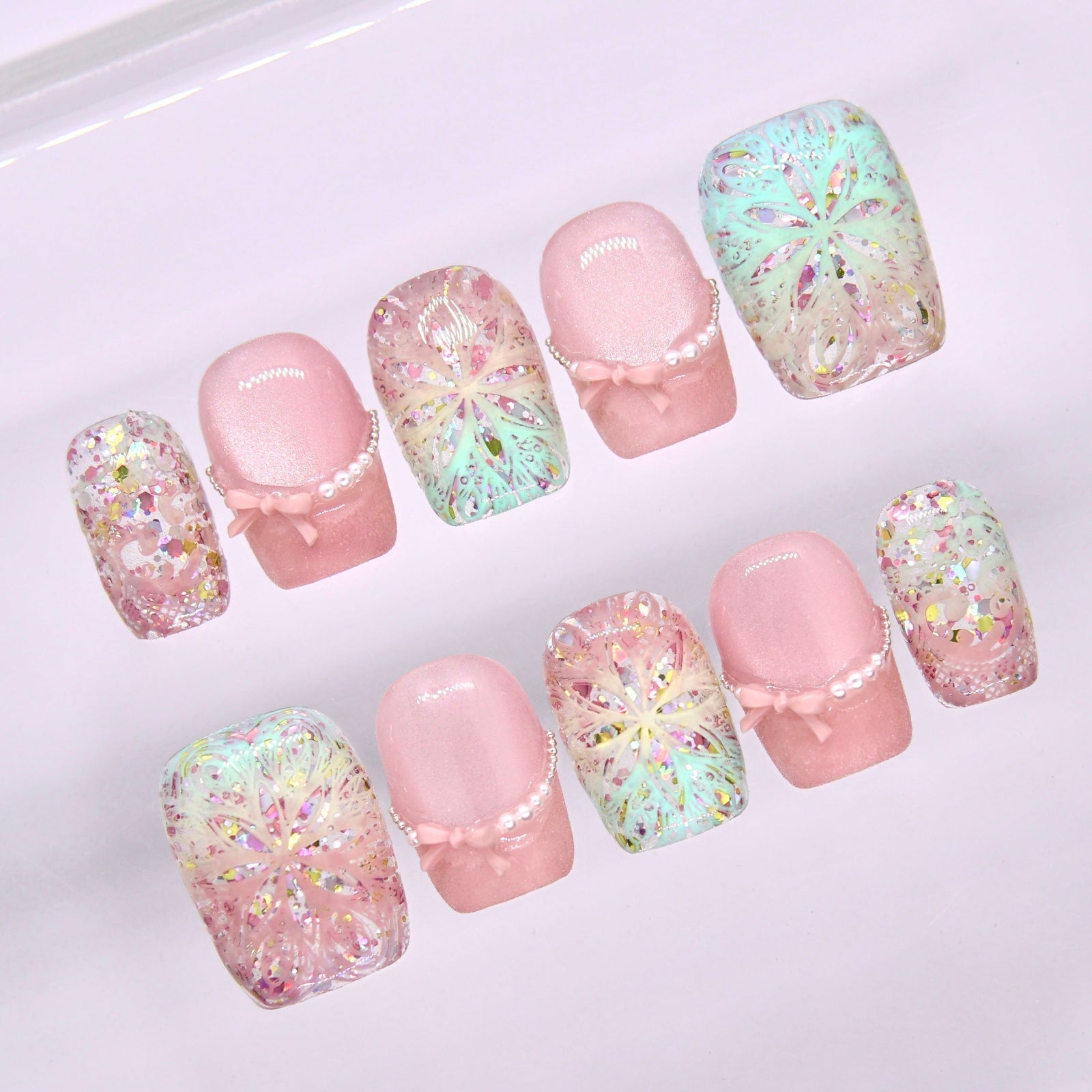 Close-up of Begin Infinite press-on nails showing kaleidoscope floral geometry in pastel mint and pink with iridescent shimmer