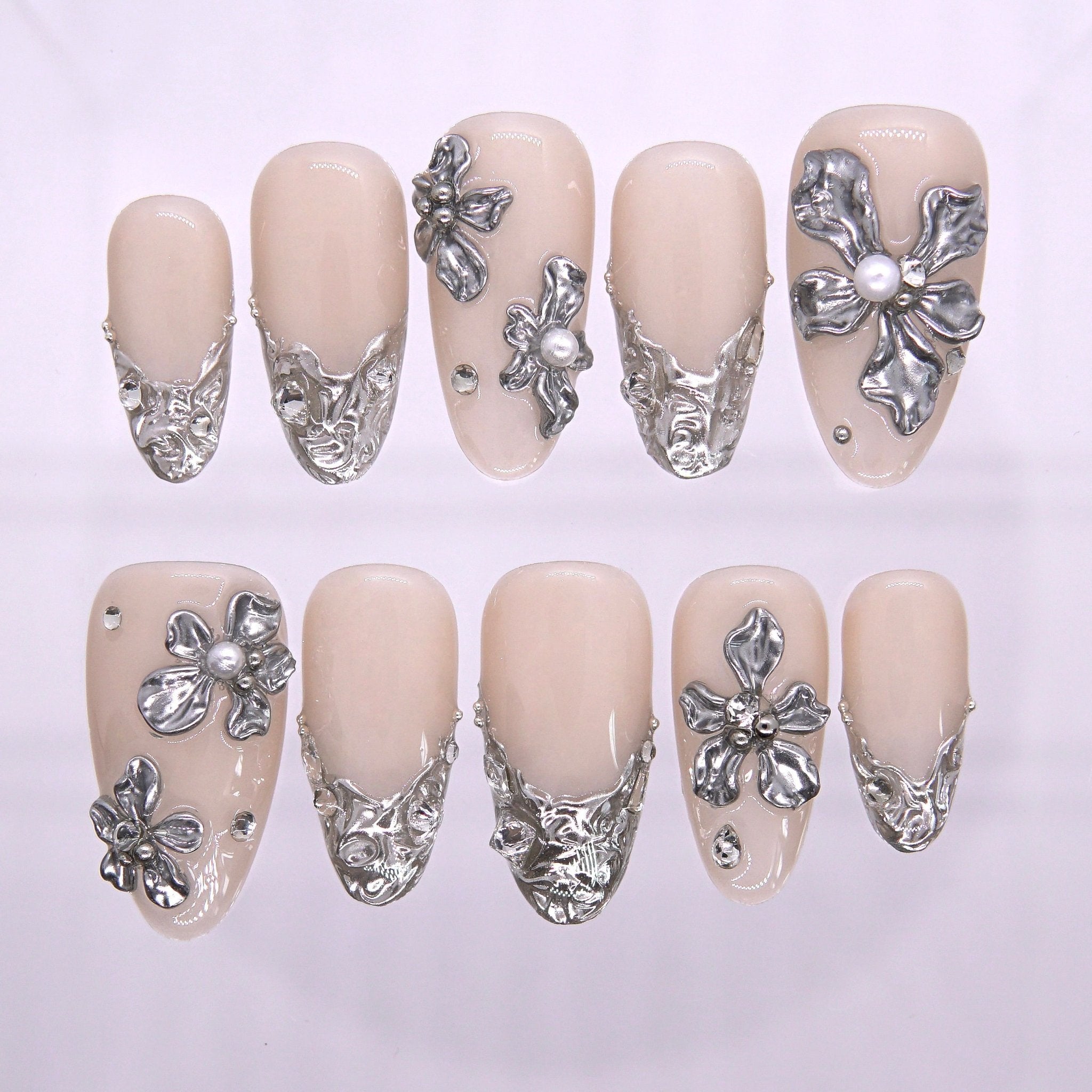 Cuvier Cliffs press-on nails laid out flat on white background, featuring creamy nude base and sculpted silver floral overlays—designed to echo La Jolla’s iconic cliffside wedding site.
