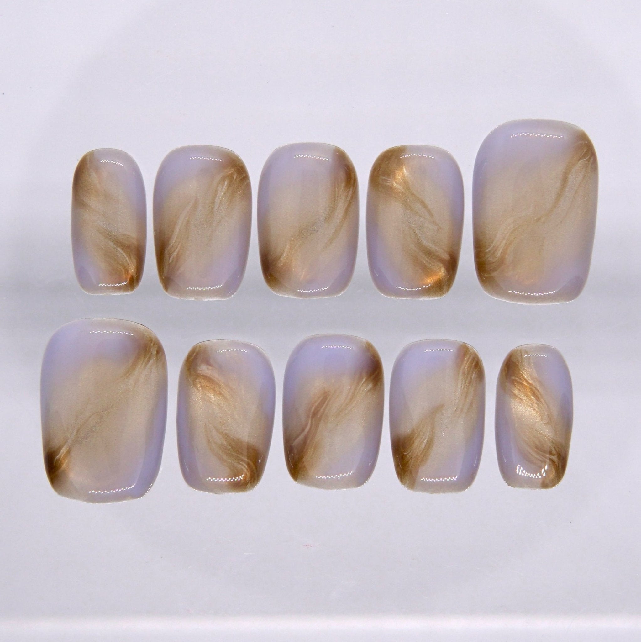 Short square press on nails with a milky nude base and soft golden brown marble swirl design on a glossy finish
