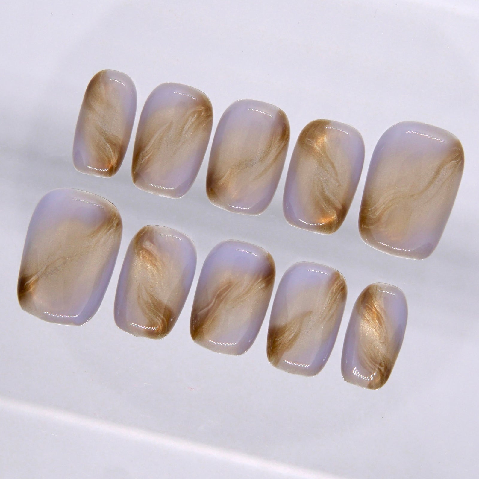 Close-up of neutral press on nails featuring flowing brown and gold marbled details over a soft translucent nude base