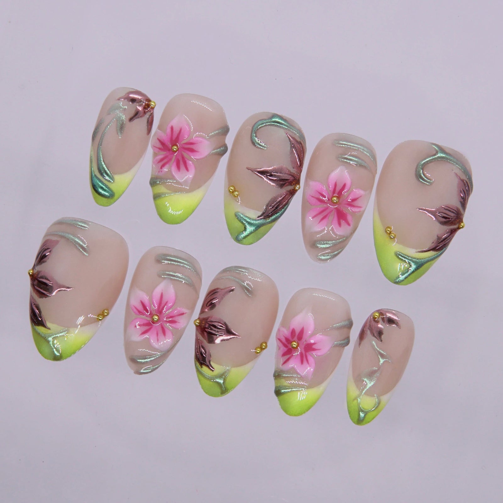 Close-up of floral press on nails featuring lime green French tips, hand-painted pink flowers, and glossy metallic chrome swirls