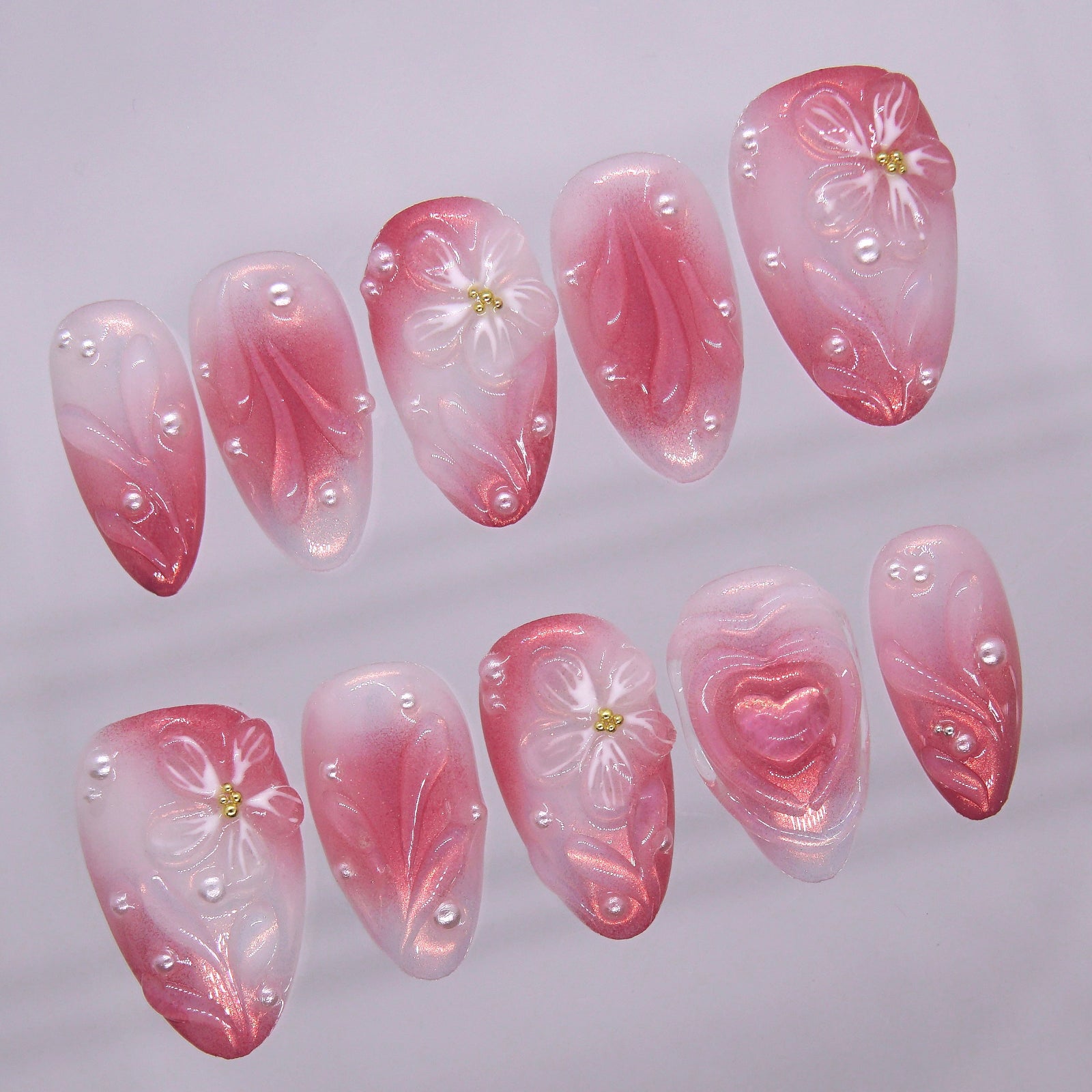 Close-up of sculpted flowers and pearls on pink gradient press-on nails.