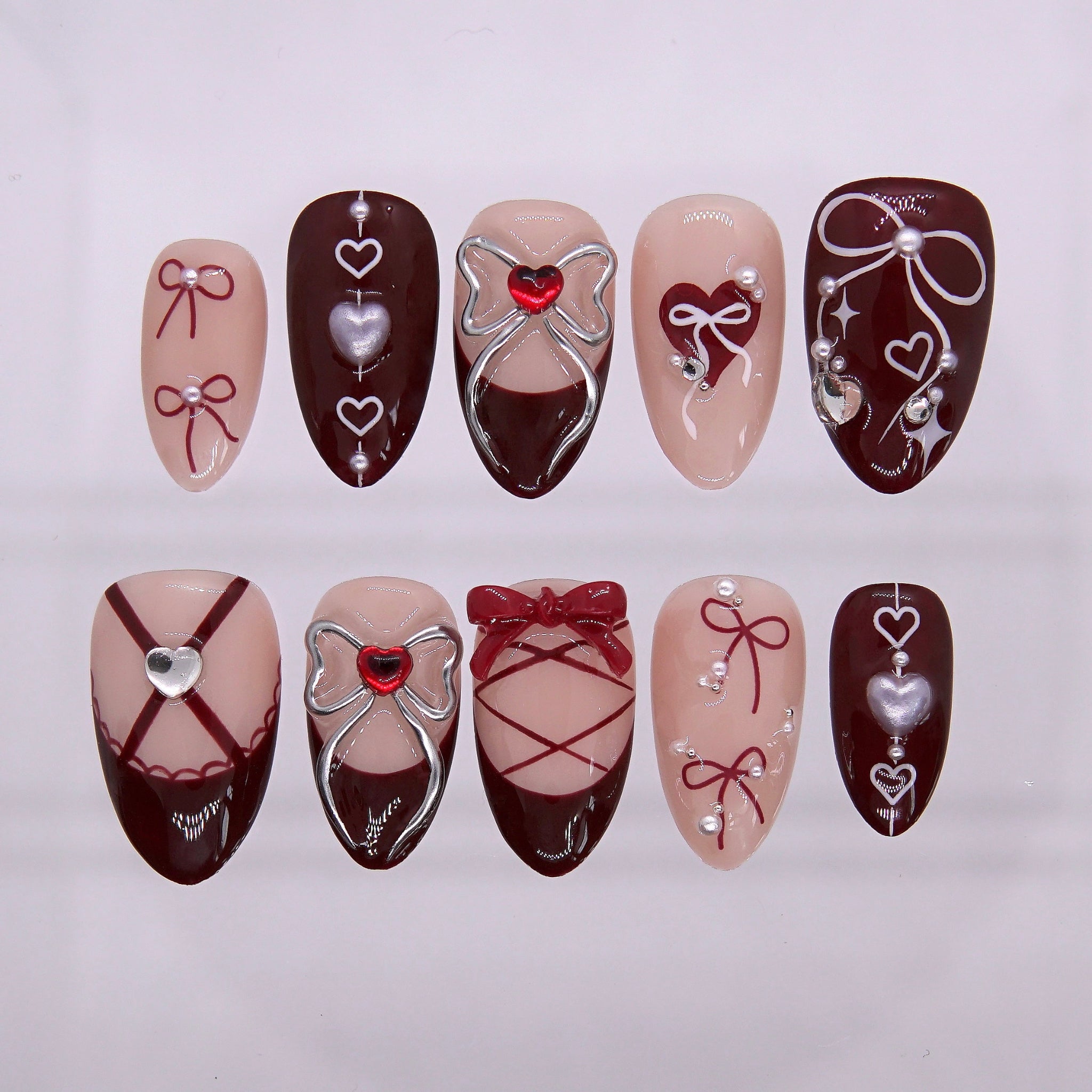 Crimson red press on nails with lace-up corset ribbon design and metallic heart accents.