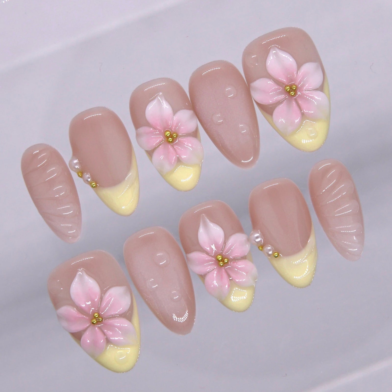 Close up of pastel yellow French tip with sculpted floral design.