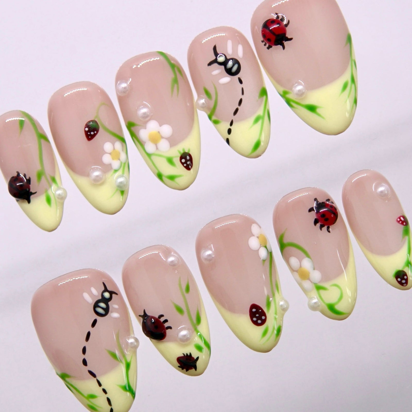 Close-up of hand-painted ladybug and flower details on sheer nude press-on nails