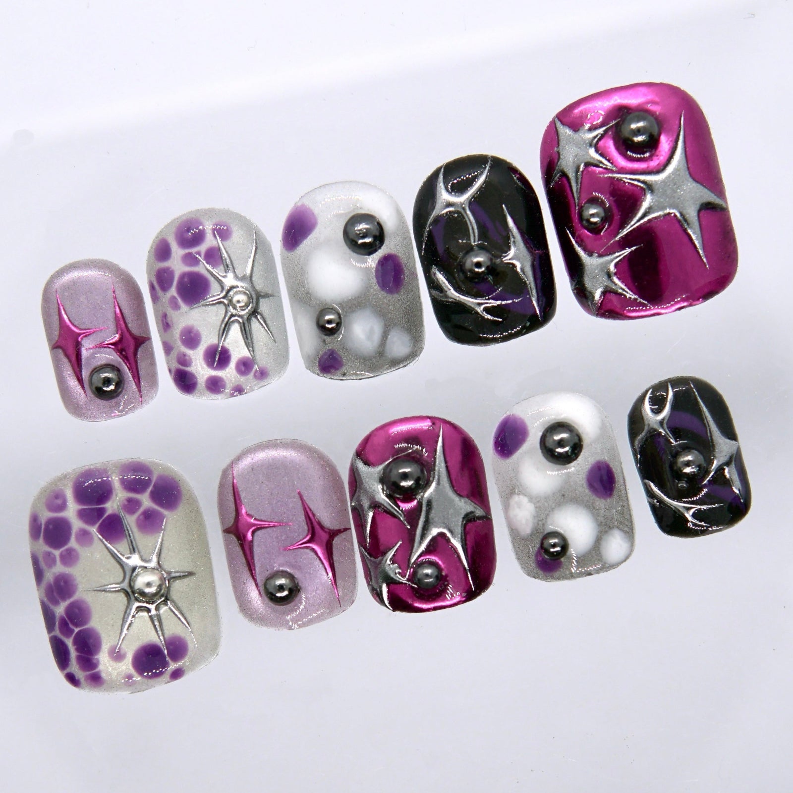 Close-up of Y2K-inspired press on nails featuring metallic pink chrome, black glossy finish, silver accents, and purple abstract details