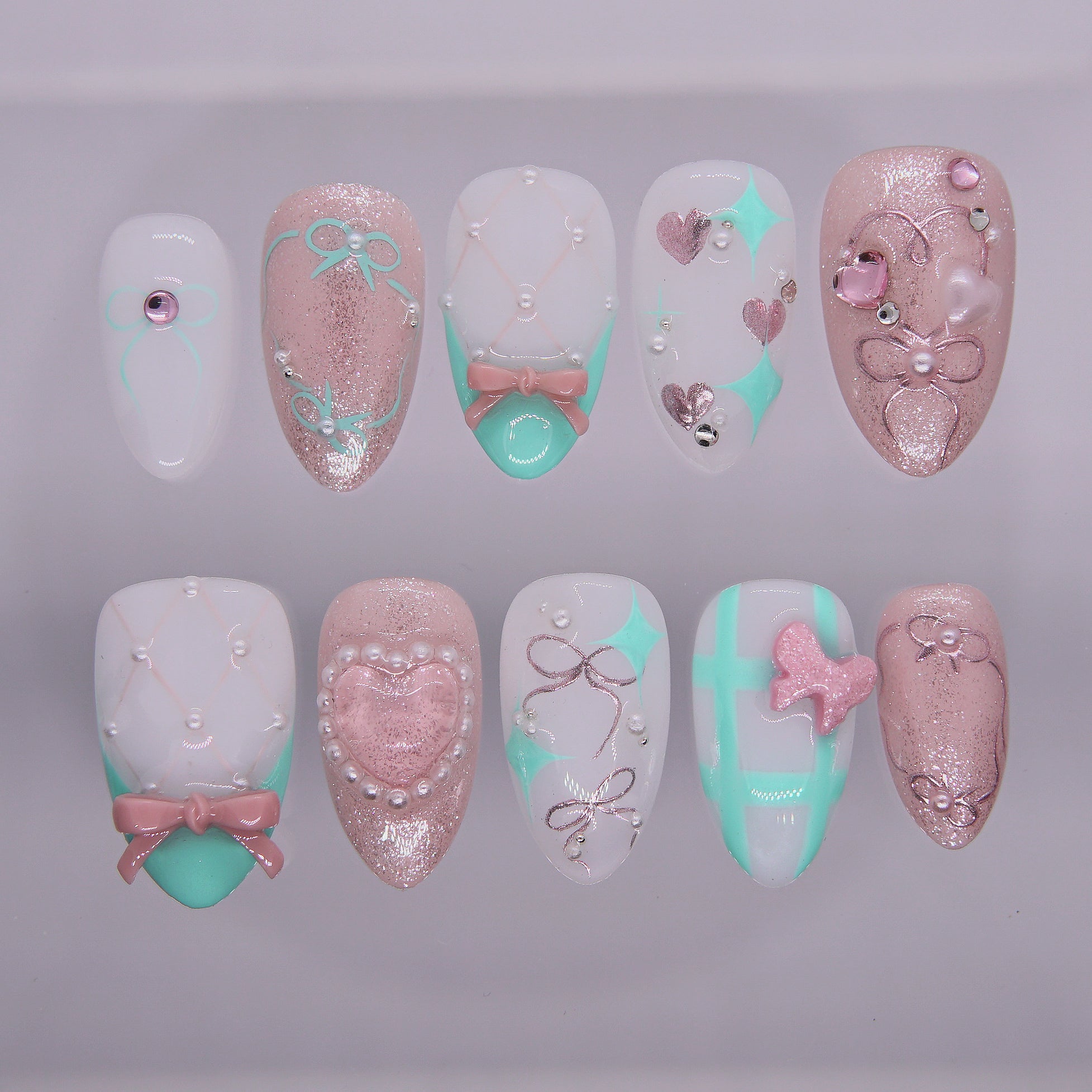 Mint green and blush pink press-on nails with 3D bows, glitter, pearls, and sculpted hearts from Nailsium’s Wood · Bloom collection.