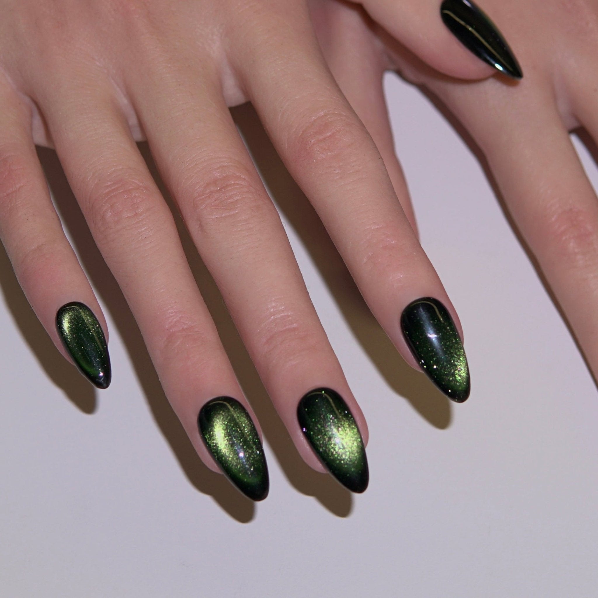 Close-up of deep green cat-eye press-on nails with golden shimmer, symbolizing growth and rebirth from Nailsium October Energy Shades.